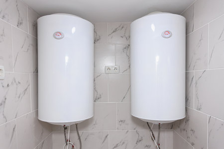 Dual electric water heaters installed on tiled bathroom wall.