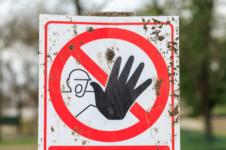 No entry sign with hand symbol and helmet graphic on weathered surface.