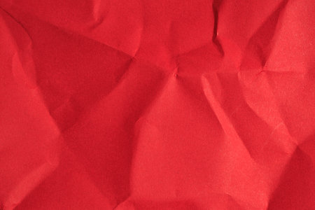 Crumpled red paper texture with folds and wrinkles.の写真素材