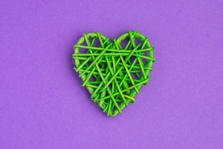 A heart made of green string is placed on a purple background. The heart is made of thin, green...