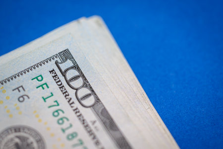 Close-up of stack of hundred dollar bills on blue background.