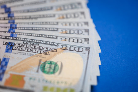 Close-up view of stacked u.s. one hundred dollar bills on blue background.