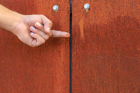 A hand pointing at a rusty door. The door is old and has a lot of rust on it, corten steelの写真素材