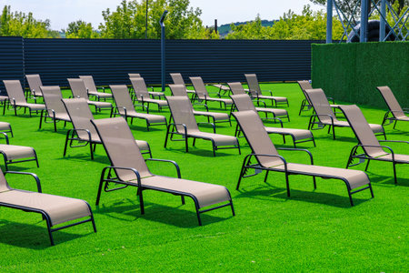A large lawn with many lawn chairs and a fence. The lawn chairs are empty and the grass is green