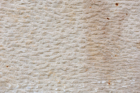 Textured beige stone wall with worn patterns and natural irregularities.の写真素材