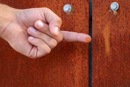A hand pointing at a rusty metal door. The hand is slightly injured, and the finger is bleeding.の写真素材