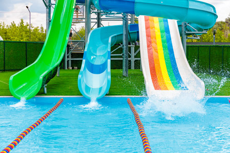A pool with three slides, one green, one blue, and one rainbow colored. The rainbow slide is in the...