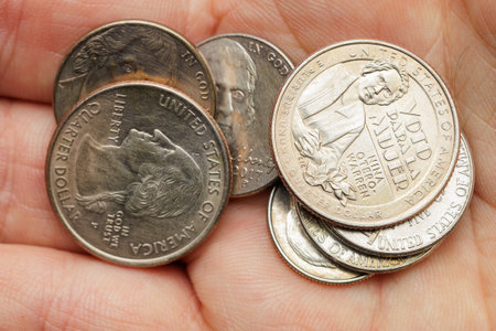 A person is holding a handful of coins, including a dime, a quarter, and a penny. The coins are all silver and appear to be from the United Statesの写真素材