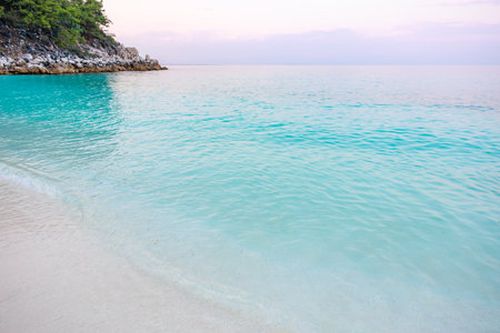 A beautiful beach with a blue ocean and a white sandy beach. The water is calm and the sky is pinkの写真素材