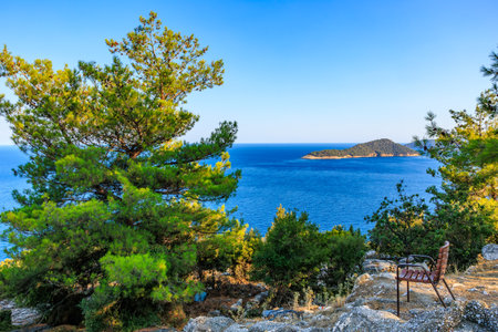A bench is sitting on a rocky hill overlooking a body of water. The scene is peaceful and serene, with the trees and water creating a calming atmosphereの写真素材
