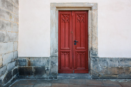 Red wooden door on stone building exterior with ornate carvings.