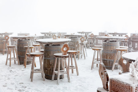 Snow-covered outdoor winter caf? with rustic wooden furniture in a misty setting.の写真素材