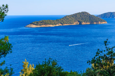 A boat is sailing in the ocean near a small island. The sky is clear and the water is calmの写真素材