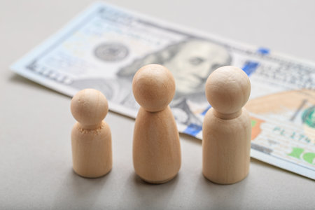 Wooden figures representing family with hundred dollar bill background.の写真素材