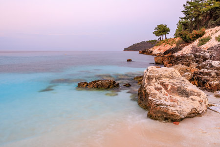 A rocky shoreline with a blue ocean in the background. The sky is a mix of pink and purpleの写真素材