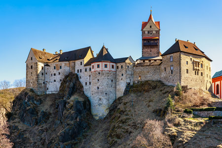 Historic medieval castle perched on rocky cliff under clear blue sky.の写真素材
