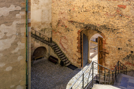 Historic stone courtyard with arched doorway and staircases in sunlight.の写真素材