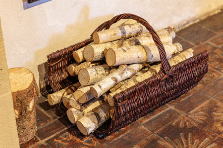 Rustic wooden basket filled with birch logs on tiled floor.