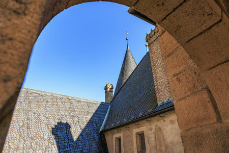 Historic castle rooftop with stone arch and spire against clear blue sky.
