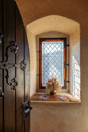 Rustic stone room with wooden door and sunlit window featuring floral arrangement.の写真素材