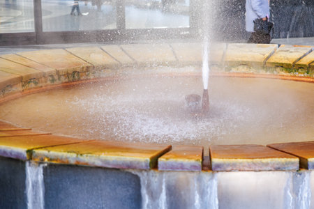 Close-up of circular fountain with flowing water in sunlit urban environment, natural geyser.の写真素材