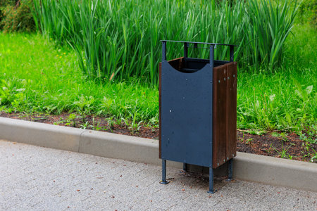 Urban outdoor trash bin by lush greenery on a paved street.の写真素材