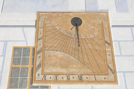 Historic sundial displaying time on weathered wall in sunlight.