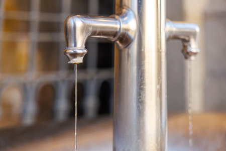 Close-up of metal water fountain spouts dripping against blurred background.
