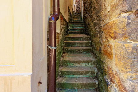 Narrow stone alley with steep steps between historic buildings in bright sunlight.の写真素材