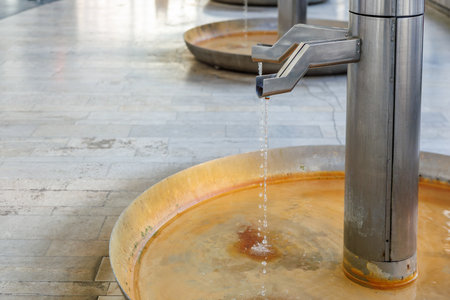 Stainless steel public fountain with flowing water and circular basins in urban setting.の写真素材