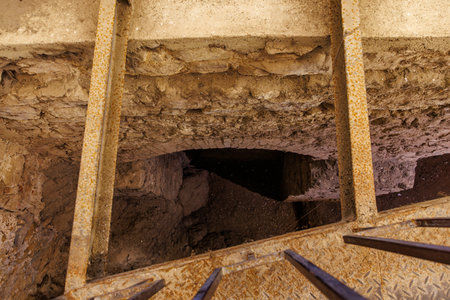 Rusty staircase overlooking ancient stone tunnel entrance.
