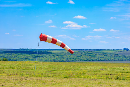 Red and white windsock on green field with clear blue sky.