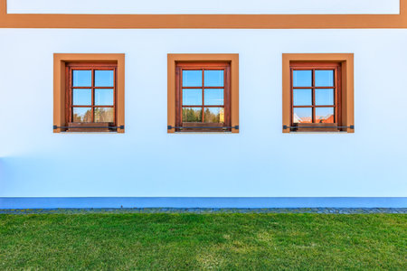 Symmetrical triple windows on white building with green grass lawn.の写真素材