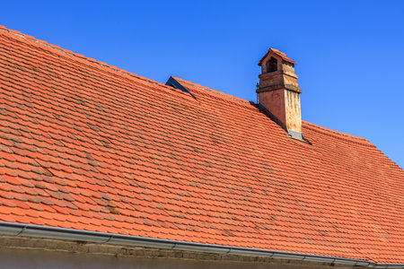 Red tiled roof with chimney under clear blue sky.の写真素材