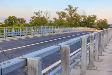Empty metal bridge with railings over road and trees in distance.の写真素材