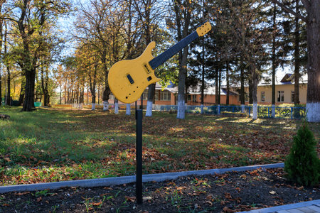 A yellow guitar is on a post in a park. The guitar is made of wood and has a black body. The guitar is placed in a grassy area with trees in the background. The scene gives off a relaxedの写真素材