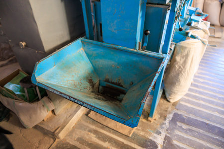 A blue machine with a blue container in front of it. The container is full of dirt