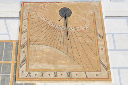 Historical wall sundial with Cesky Krumlov and arabic numerals in sunlit stonework design.