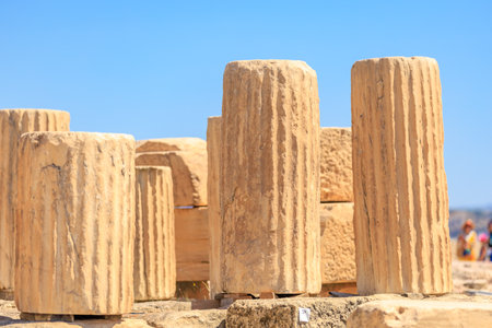 A group of stone pillars are standing in a field. The pillars are tall and brown, and they are arranged in a row. The sky is clear and blue, and there are a few people in the backgroundの写真素材