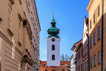 Baroque church tower between historic buildings against blue sky.の写真素材