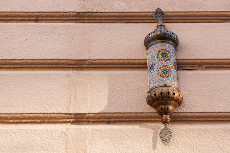 Ornate mosaic lantern against textured wall on sunlit day.の写真素材