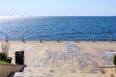 Sunny waterfront promenade overlooking serene blue ocean on a clear day.の写真素材