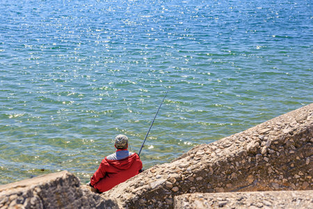 Elderly caucasian male fishing by the seaside in bright sunlight.の写真素材