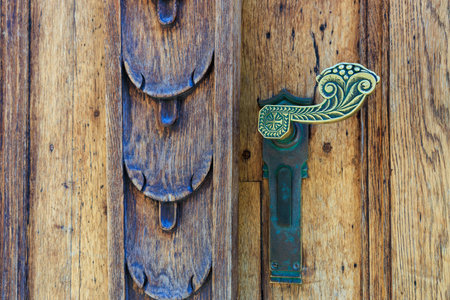 Ornate brass door handle on rustic wooden door with decorative carving.の写真素材