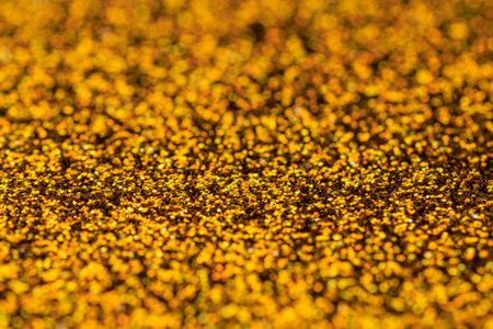 The image is a close up of a gold glittery surface. The gold color is very bright and shiny, and the glitter adds a sense of movement and energy to the scene. Scene is one of excitement and joyの写真素材