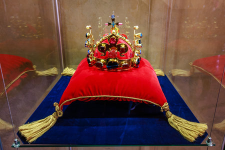 Ornate royal crown on red cushion with gold tassels in glass display case.の写真素材