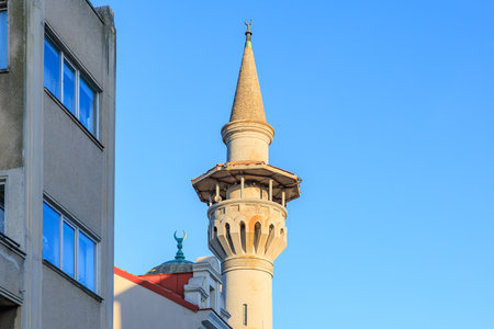 Historic minaret and urban architecture against blue sky.の写真素材