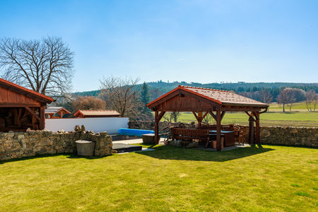 Rustic wooden gazebo in scenic countryside with stone fence and lush greenery.の写真素材