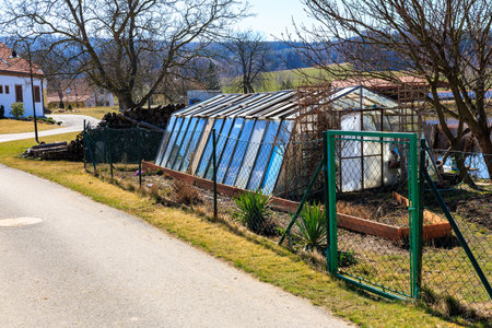 Rural garden greenhouse with metal fence in countryside setting.の写真素材
