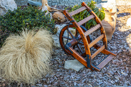 Rustic wooden wheelbarrow in garden with dry grass and clay pot.の写真素材